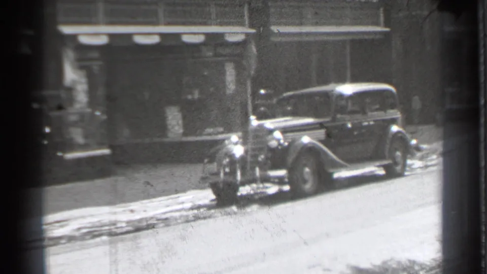 A 1930s sedan sits along the curb outside storefronts in Danielson, Connecticut, with snow visible on the sidewalk edge.