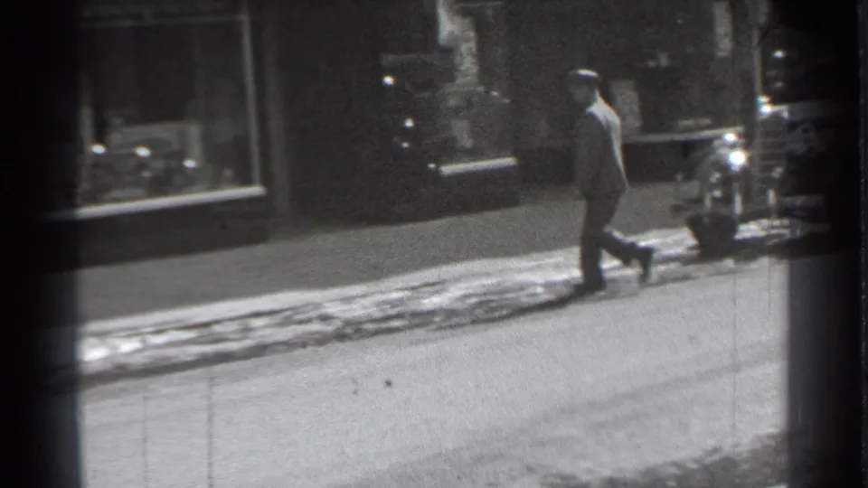 In 1939 Danielson, Connecticut, a man in a hat walks past shop windows beside a snow-lined curb.