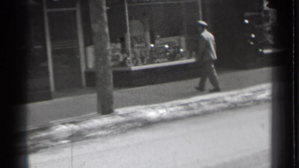 The walking man passes a utility pole and display window on a snowy Danielson sidewalk in the 1939 home movie.