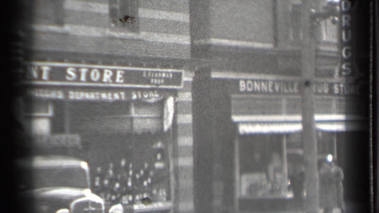 Street storefronts with Bonneville Drug Store signage, parked car, and pedestrians on the sidewalk.