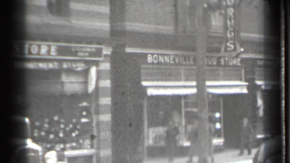 Danielson storefront view showing Bonneville Drug Store, sidewalk pedestrians, display windows, and the edge of a vintage automobile.