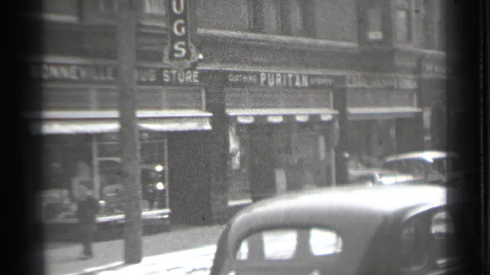 Danielson, Connecticut downtown storefronts in 1939, with pedestrians walking below shop signs and vintage automobiles along the street.
