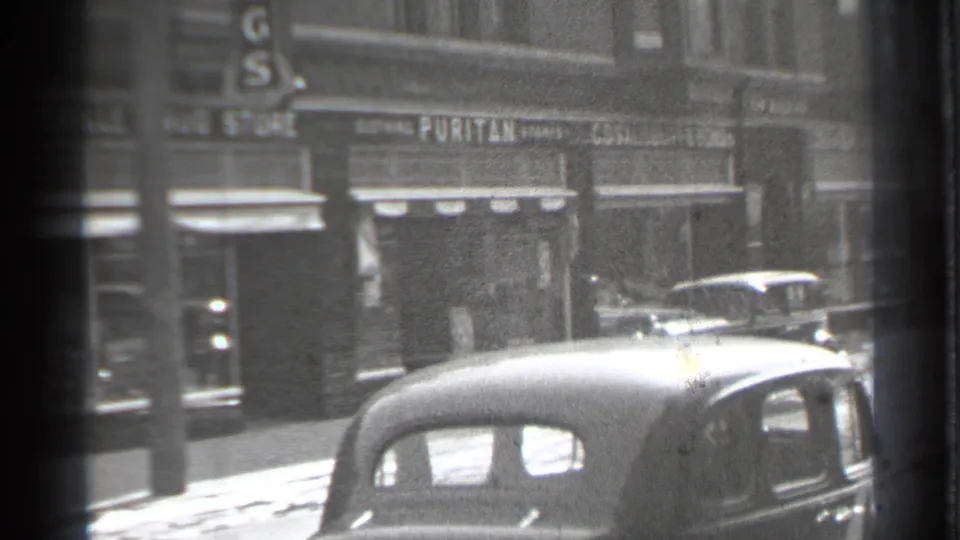 Final 1939 Danielson street frame showing shopfronts with Puritan signage, pedestrians, awnings, and parked automobiles in a small downtown block.