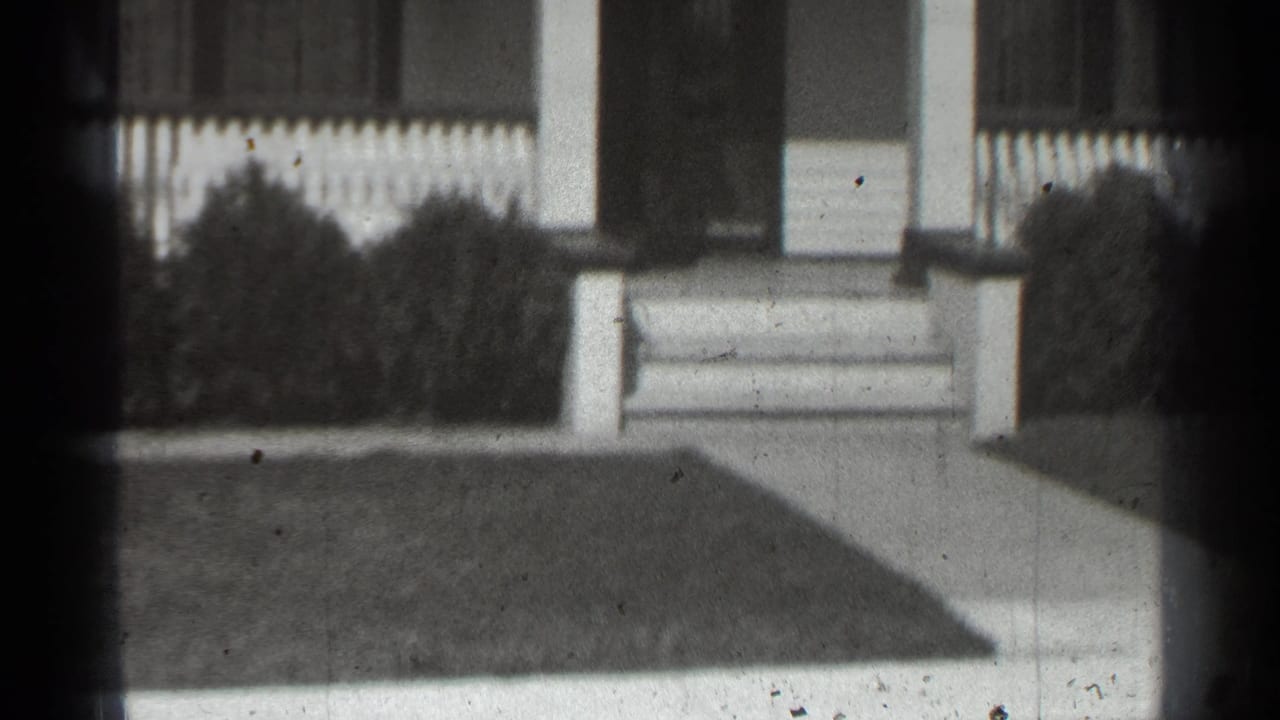 House entrance with porch posts, steps, fence, bushes, walkway, and clipped lawn.