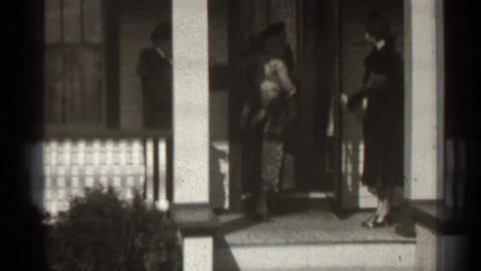 A woman stands in the doorway as another woman in a dark coat waits on the porch of a New York home in 1939 footage.