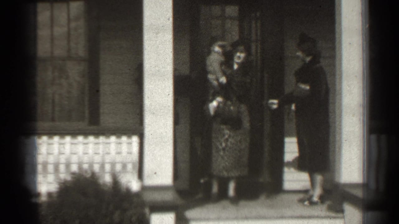 In a supplied 1939 New York home-movie frame, women gather on a columned porch as one holds a baby near the doorway.