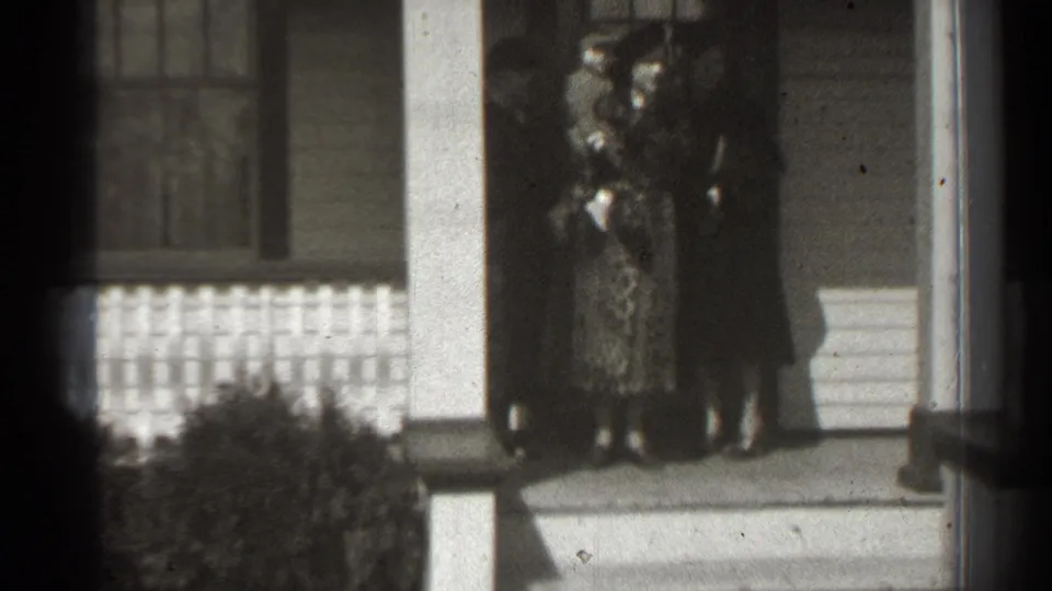 Women stand close together on a New York porch in the supplied 1939 clip, with a baby held near the front entrance.