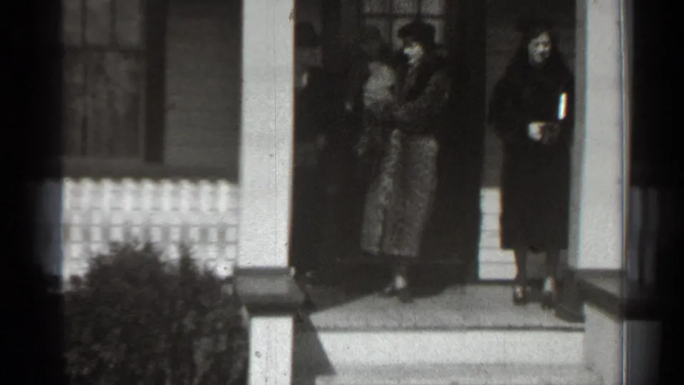 At the end of the supplied 1939 New York porch scene, a woman holds a baby near the doorway as another woman stands to the side.