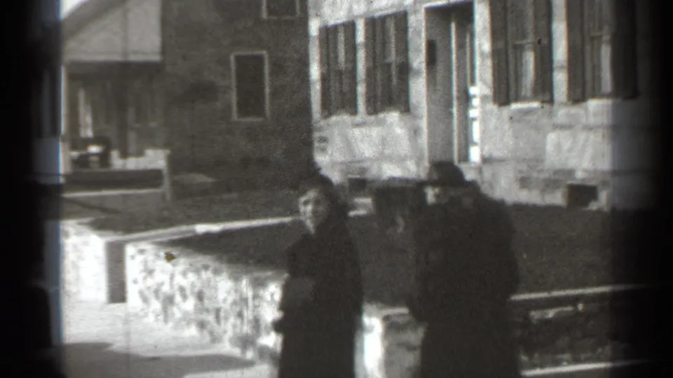 Two women in 1930s-style coats and hats walk past stone walls and residential buildings in New York, based on clip metadata.