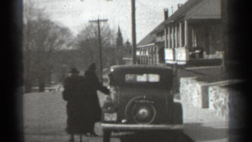 One adult appears to reach for or open the car door as another stands close by on the residential street.