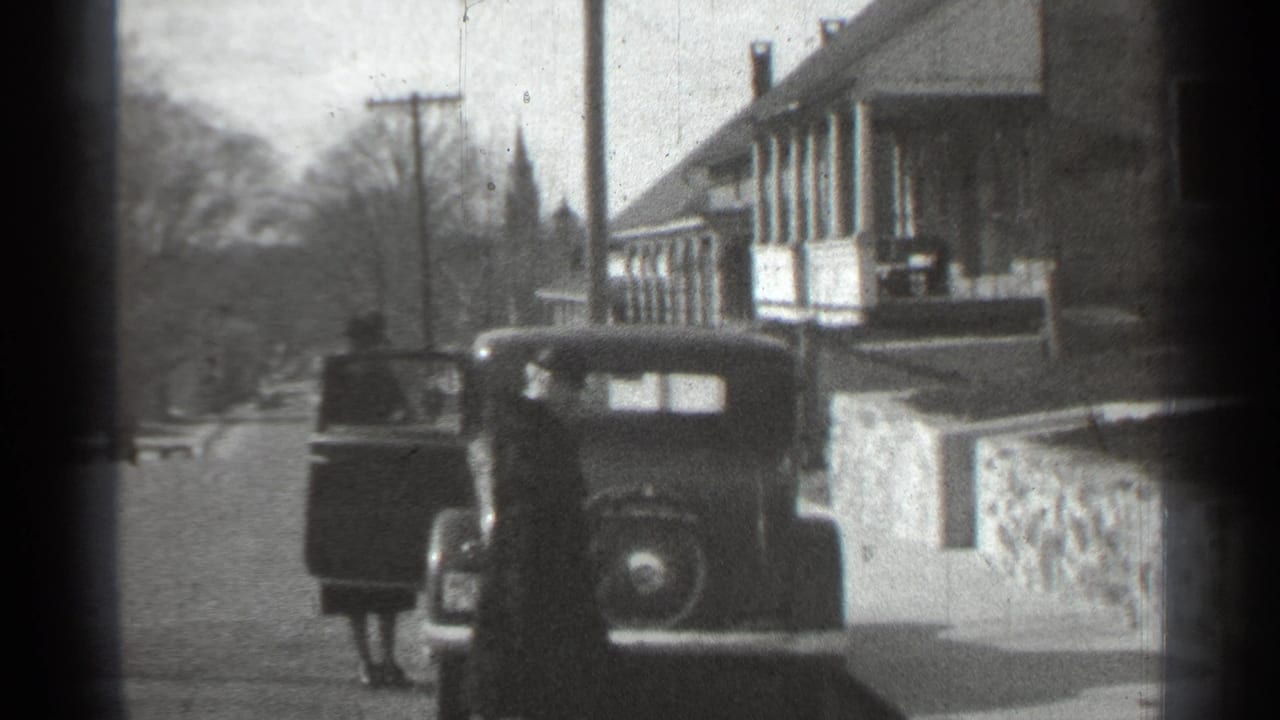 Older car parked beside a building while a person stands at the open door.