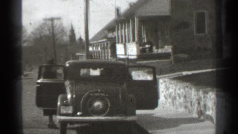 Late-1930s New York home-movie frame of a classic car with doors open along a quiet suburban block.