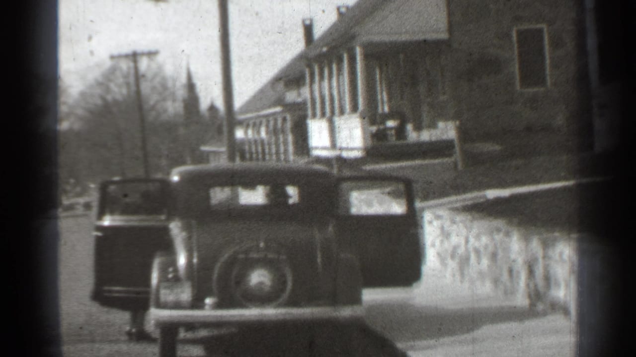 Rear view of a parked car with both doors open near houses and a stone wall.