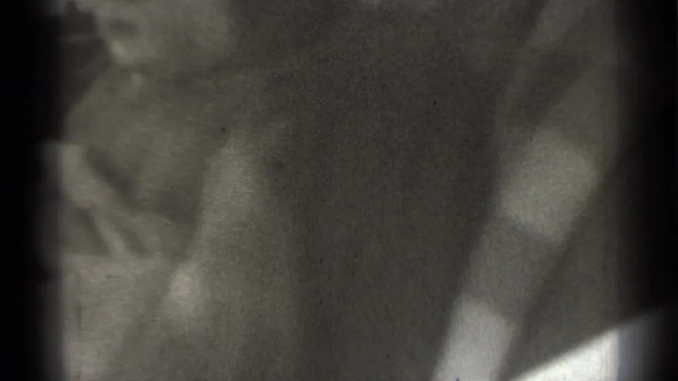 Soft, obscured 8mm frame with a person close to the camera and the street scene largely blocked.