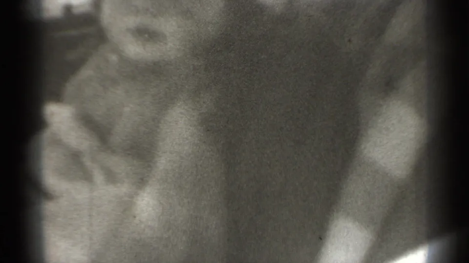 1939 home-movie frame with a blurred person close to the lens, partially showing a face and coat while blocking the background.