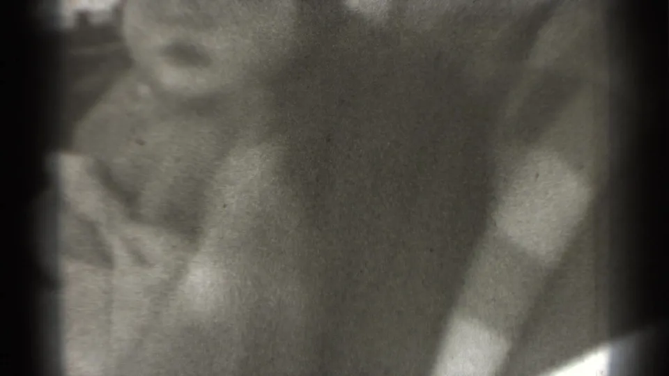 Grainy 1939 New York 8mm frame showing a young child in a light cap looking near the camera.