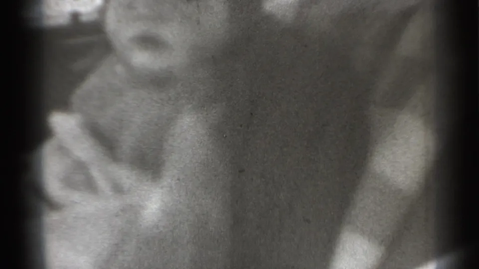 Close 8mm frame of a young child in a cap, with a small string-like object visible near the face.