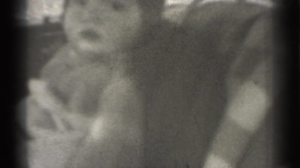 Soft, grainy 8mm frame of the child turning slightly within a tight home-movie close-up.