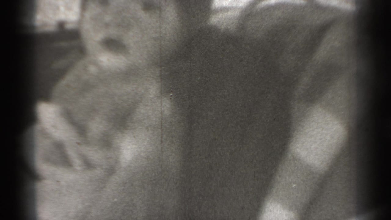 Grainy 1939 New York 8mm frame of an infant in light clothing seated in a car interior, with window light behind.