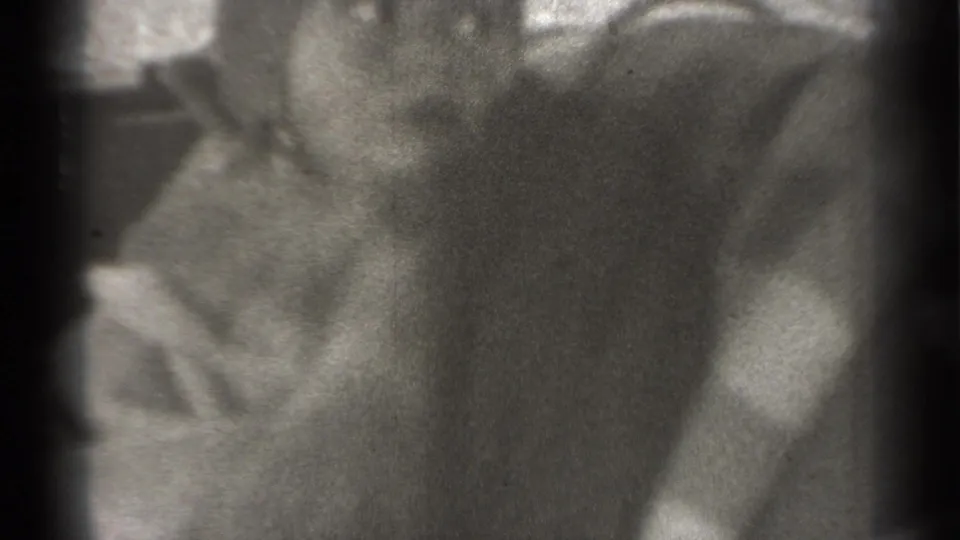 Close black-and-white 8mm view of an infant seated inside a vehicle in New York, with the figure turned slightly away.