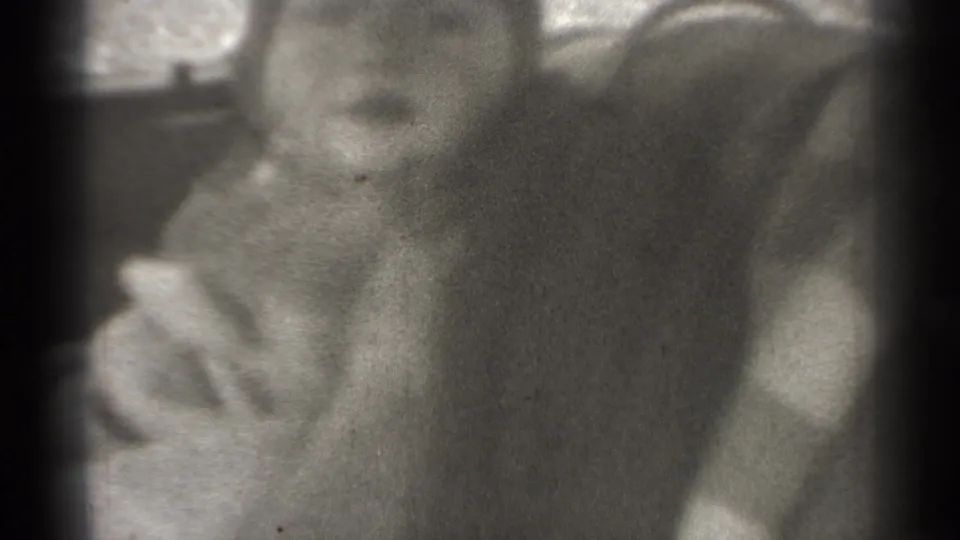 Soft 1939 home-movie frame showing an infant in a vehicle, with the child's head turned and exterior light through the window.