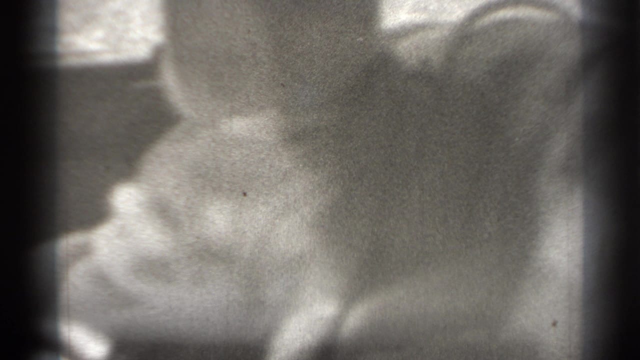 Soft black-and-white close-up of a baby seated against a dark cushion.