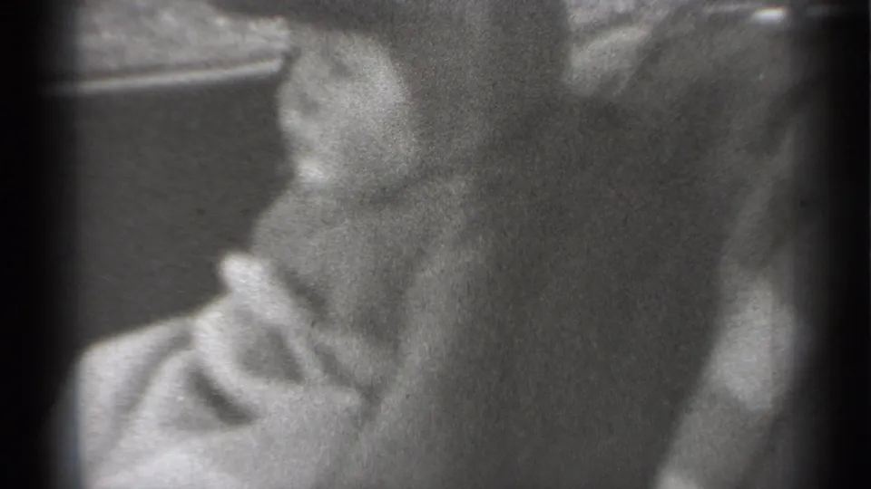 The baby appears in profile inside the vehicle setting, with a partial adult figure or arm near the right edge.