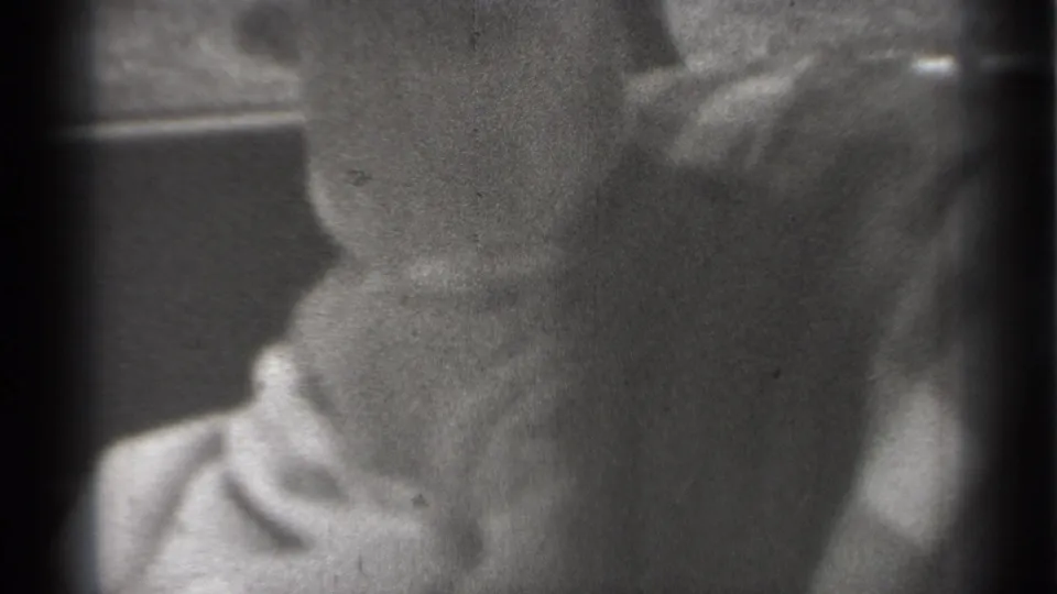 1939 New York frame of a baby seated in a car, face partly visible beneath a light cap or bonnet near the window area.