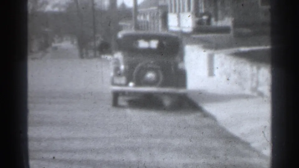 Soft black-and-white 8mm view of a vintage automobile idling or stopped by the curb on a New York street in 1939.
