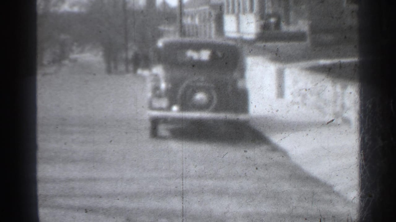 Soft 8mm frame of a vintage car parked beside a residential sidewalk.