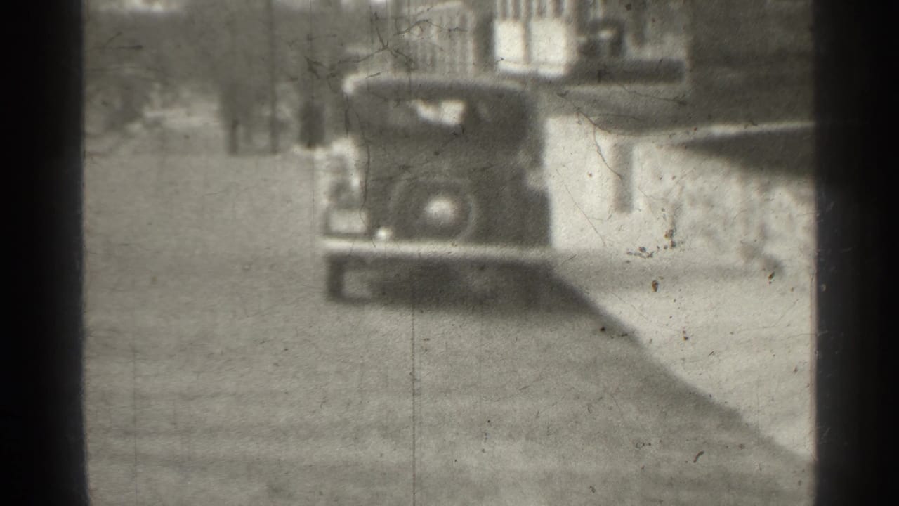 Parked vintage car seen closer against a wall and residential building.