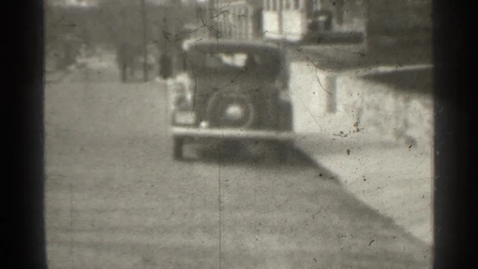 1939 New York street view with a parked vintage automobile, low wall, sidewalk, and soft monochrome 8mm texture.
