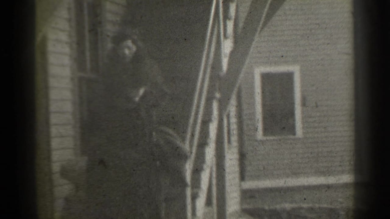 Two women in dark coats stand near exterior stairs beside a clapboard house.