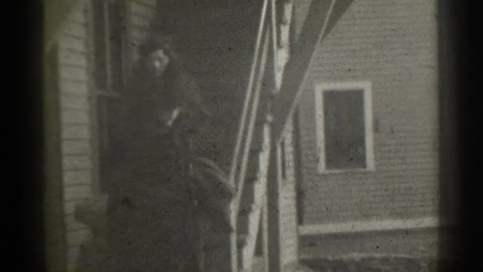 In 1939 New York home-movie footage, two women in dark fur coats and hats are near outdoor stairs beside a wooden house.