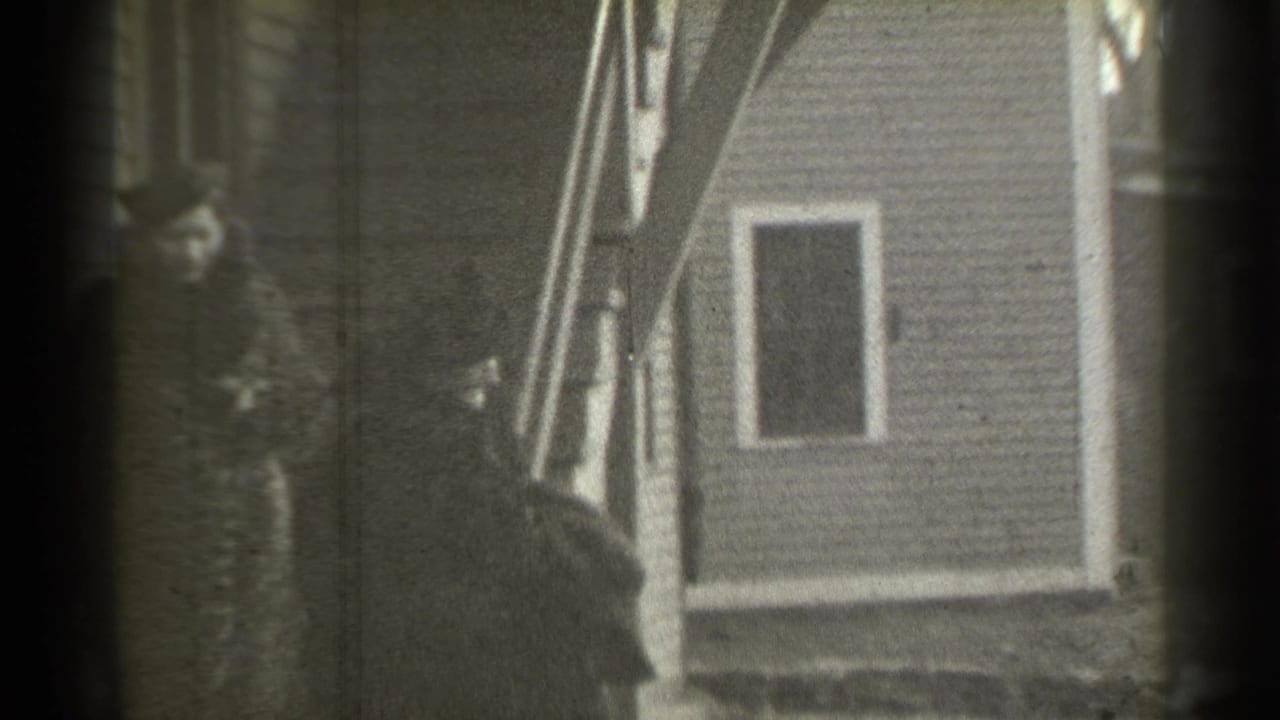 A woman in a dark coat stands on exterior steps while another figure is lower in frame.