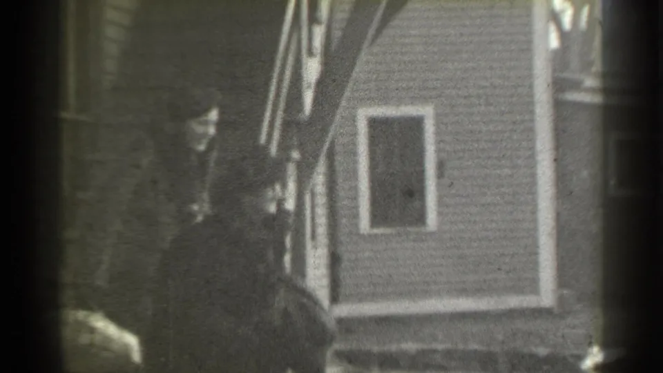 Two women in dark fur coats and hats are visible near the stairway of a New York house, one appearing to carry luggage.