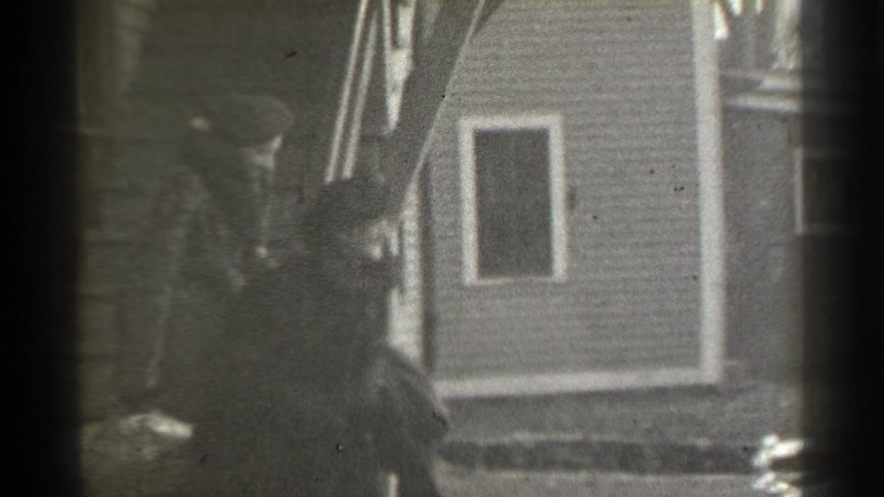 Woman near a house exterior, partly obscured by film-frame borders.