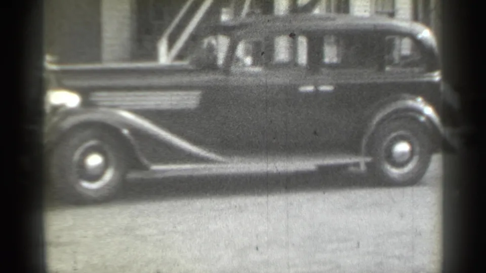 1939 New York frame with a dark sedan in profile, rounded fenders, running board, windows, and exterior stairs behind it.