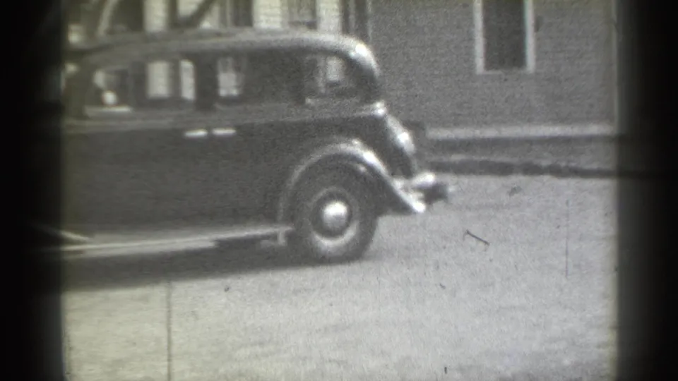 1939 New York frame showing the sedan's rear section moving out of view along a quiet residential street with dark film edges.