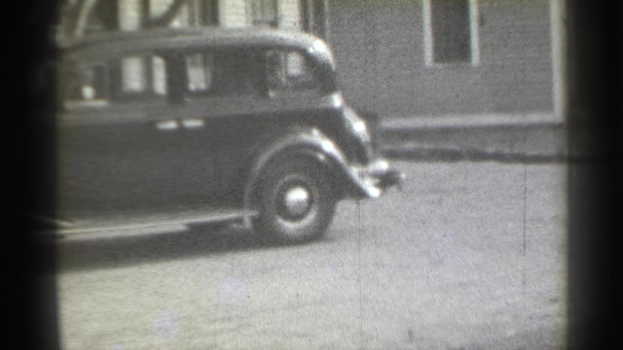 Partial view of a dark rounded sedan parked along a city street.