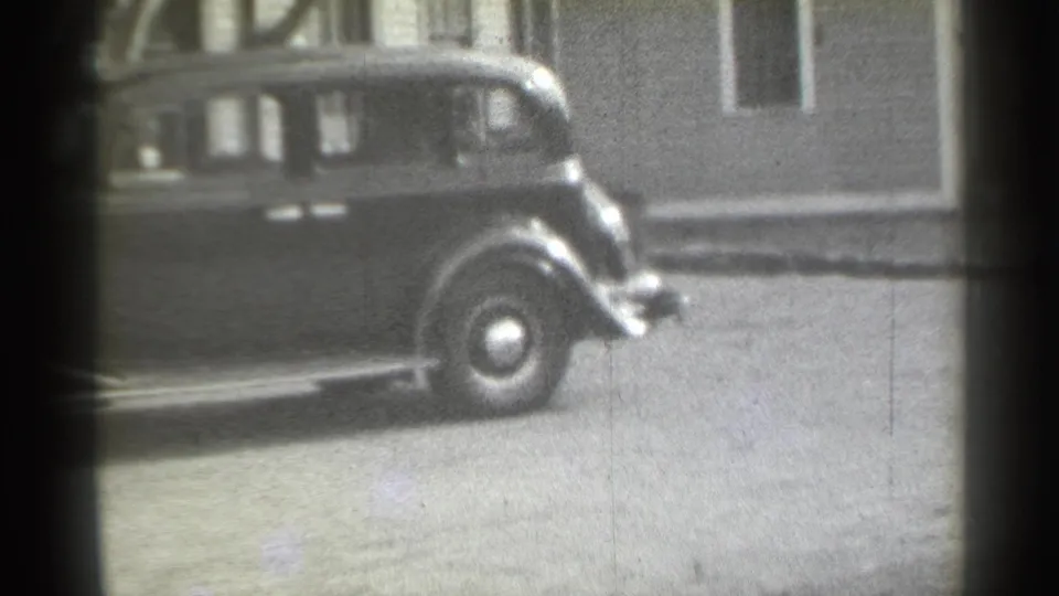 1939 New York 8mm frame showing the rear half of a dark pre-war sedan beside building fronts.