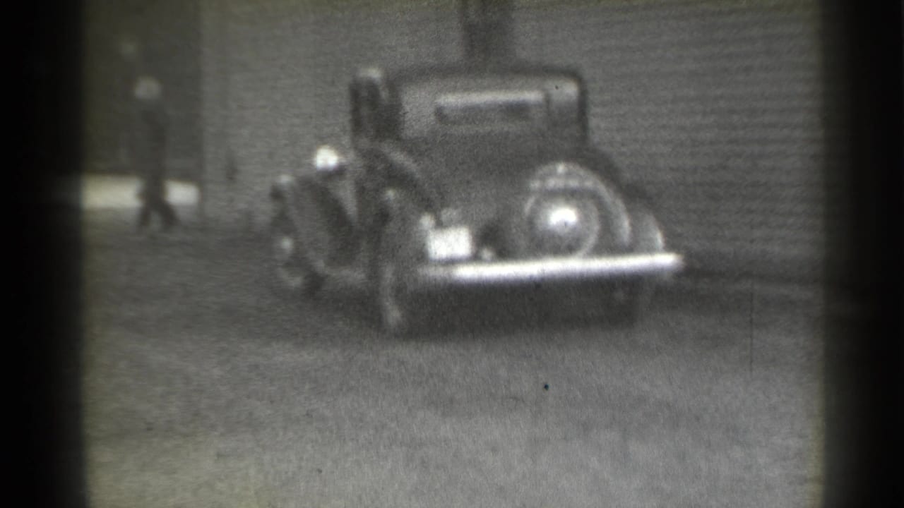 Dark car parked near a building while a pedestrian walks in the background.