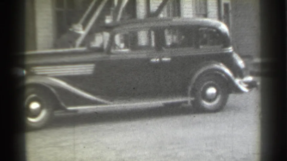 1939 New York street frame showing a dark sedan parked curbside, with faint figures visible through or near the side windows.