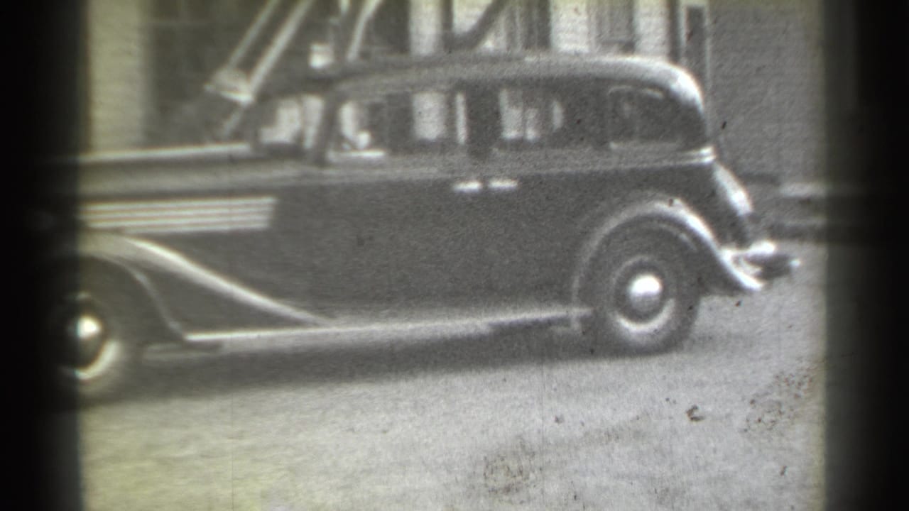 1939 New York home-movie frame showing a dark sedan in profile along an urban alley with soft 8mm film grain.