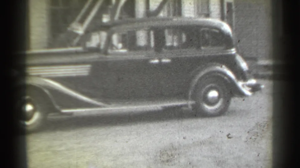 1939 New York home-movie frame showing a dark sedan in profile along an urban alley with soft 8mm film grain.