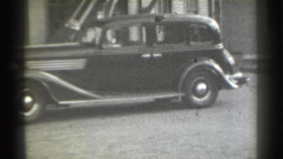 Dark 1930s sedan parked in a New York alley, seen through soft focus and dark 8mm frame edges.