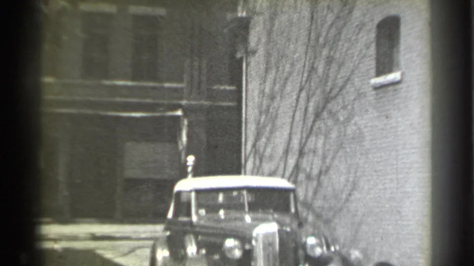1939 New York alley view with the dark sedan facing the camera between masonry walls and bare branches.