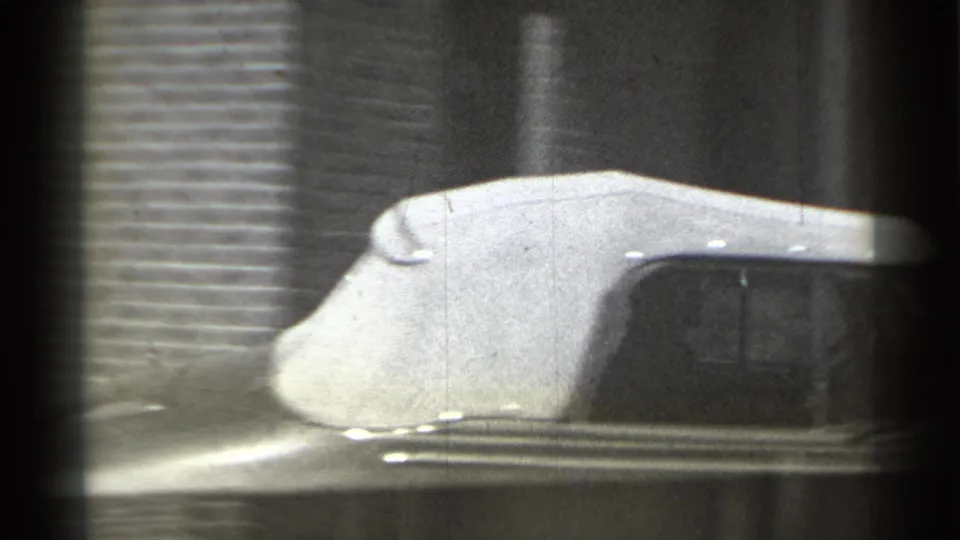 Close 8mm frame of the convertible's pale fabric roof and windshield area as the car passes close to the camera in New York.