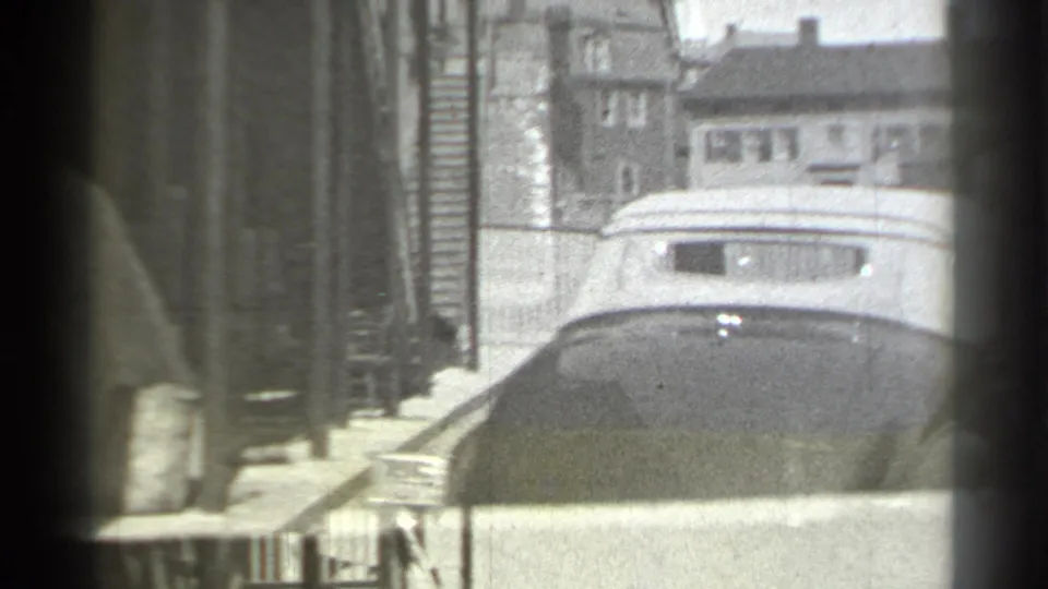 Rear view of the vintage convertible on a New York street, with railings, brick walls, and distant residential buildings in the background.