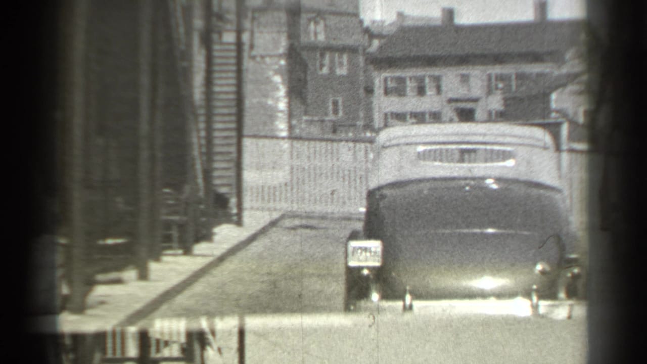 Dark convertible driving toward the camera on a residential street.